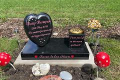 Heart-shaped black granite headstone with red floral arrangements